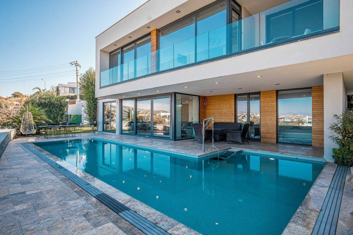 Une maison moderne à deux étages, dotée d’une piscine, de grandes baies vitrées et d’un espace salon extérieur.