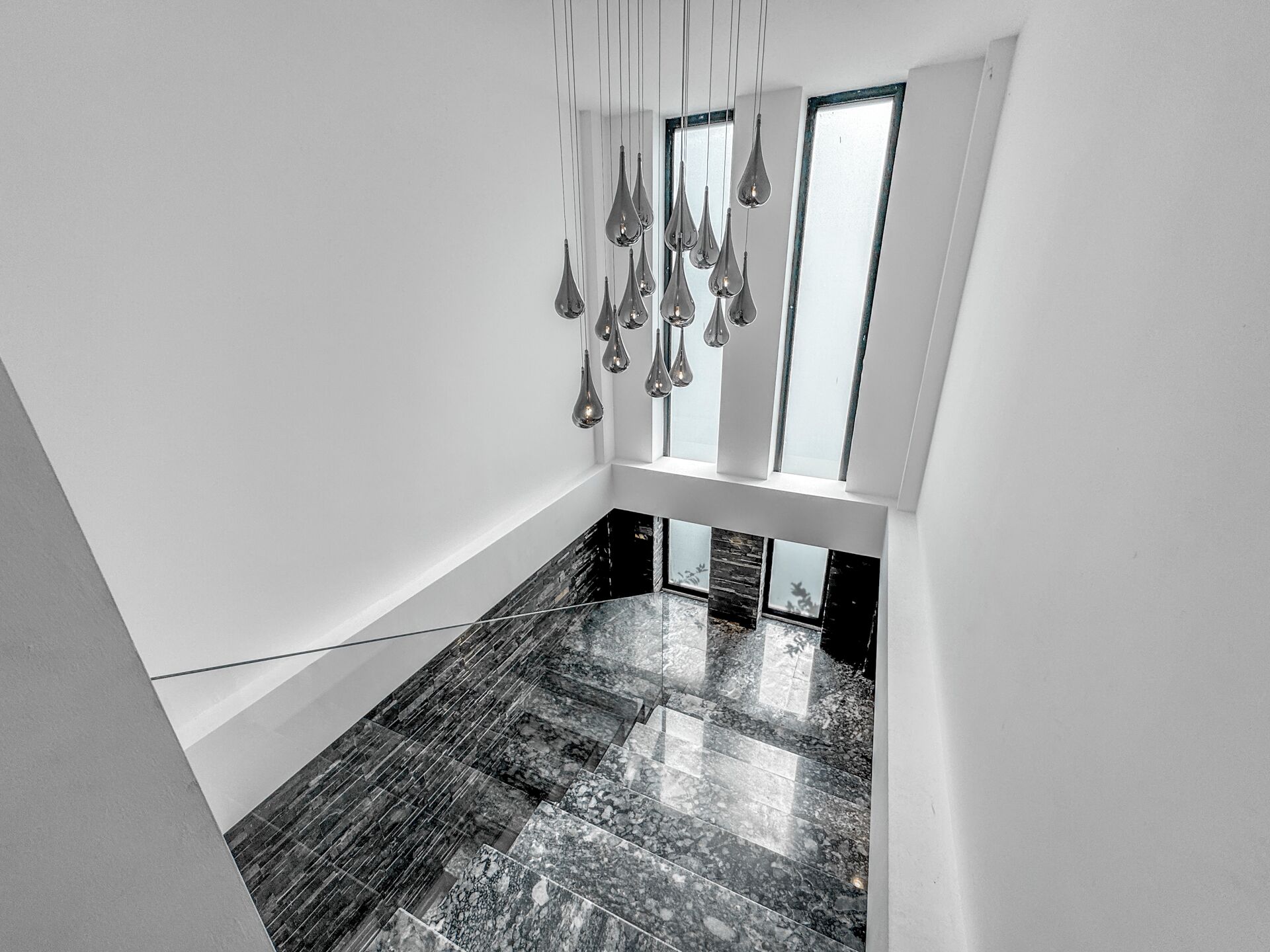 A modern interior with a marble floor, a hanging light fixture, and a window with a view.