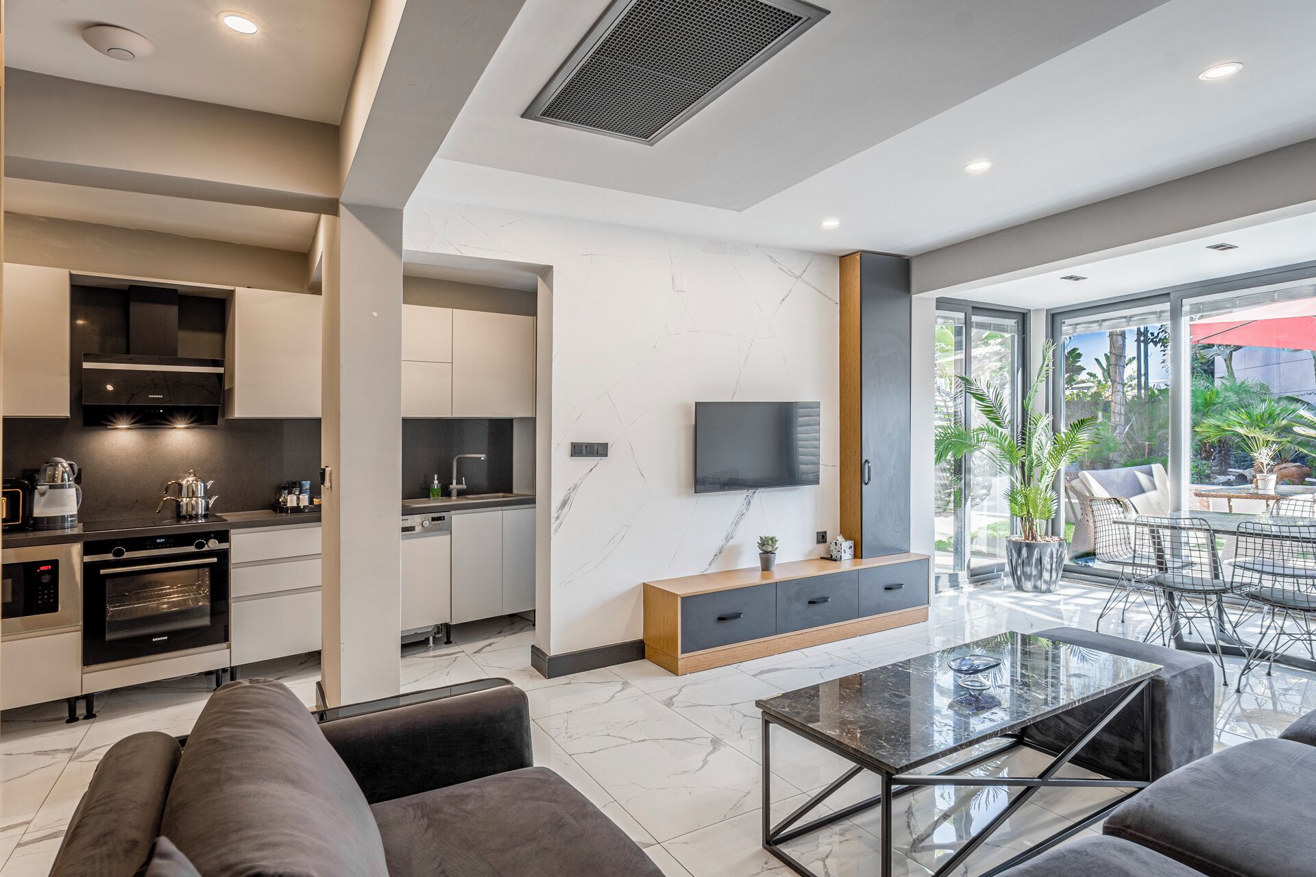 A modern kitchen with built-in appliances, a dining area with a glass table, and a view of the outdoors.