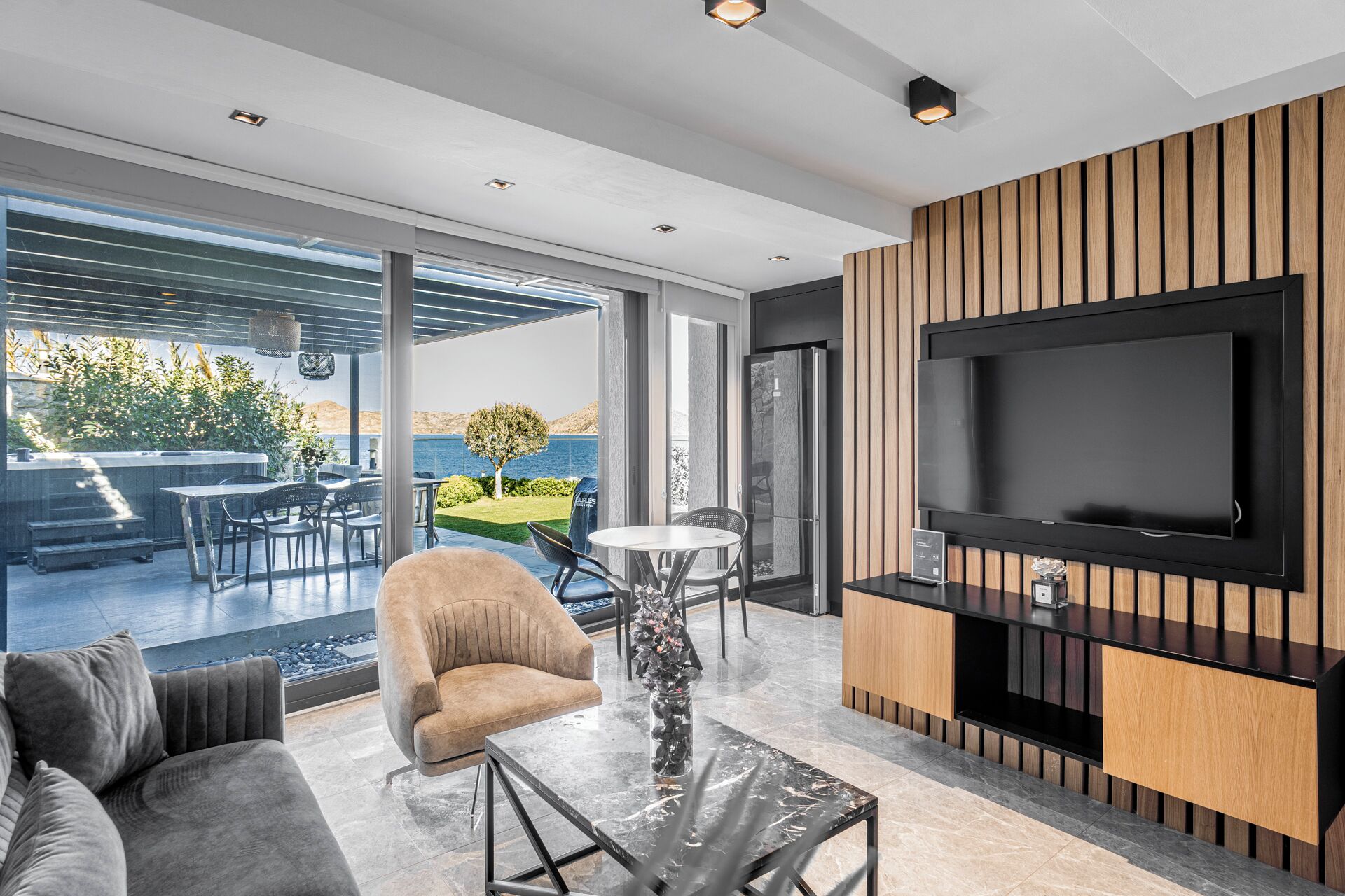 A modern living room with a large TV, comfortable seating, and a view of the outdoors.