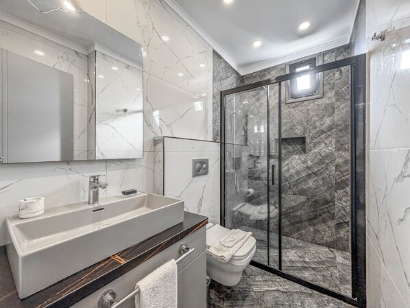 A modern bathroom with a large sink, mirror, and glass shower enclosure. - Çimentepe Residence Deluxe. (Bodrum)