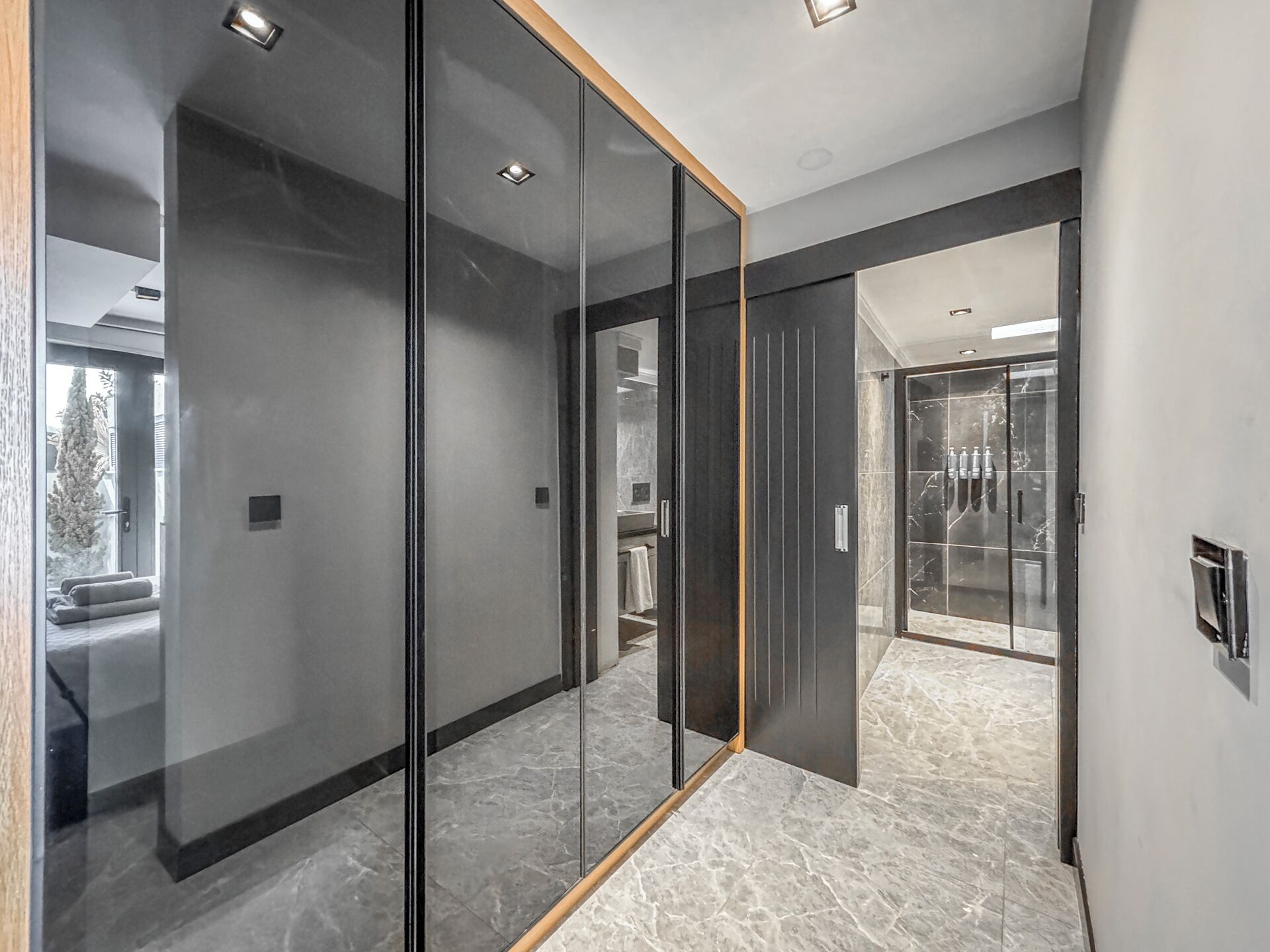 A modern interior with a glass partition, a marble floor, and a visible bathroom with a shower.