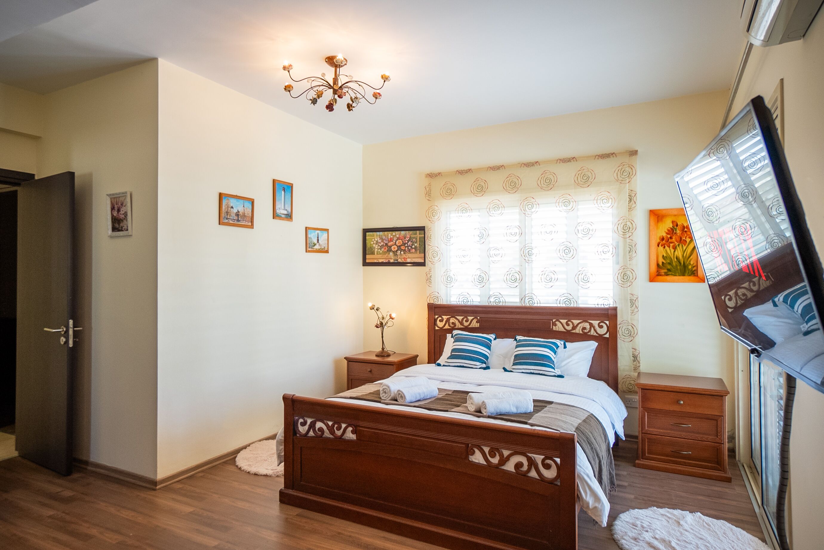 A bedroom with a wooden bed, a nightstand, a dresser, a TV, and a window with curtains.