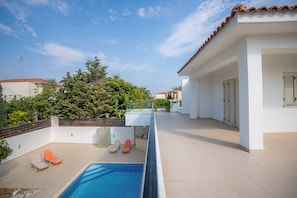 A rooftop pool area with a clear blue pool, two orange lounge chairs, and a white building with a tiled roof. - Beachfront 3 BDR Villa With Pool (Pyla)