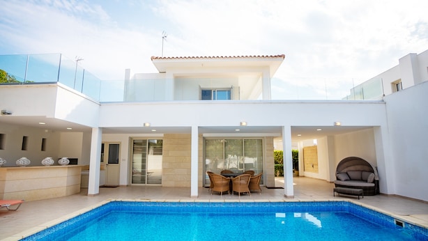 Een modern huis met een zwembad, een eethoek met buitenmeubilair en een overdekt terras.