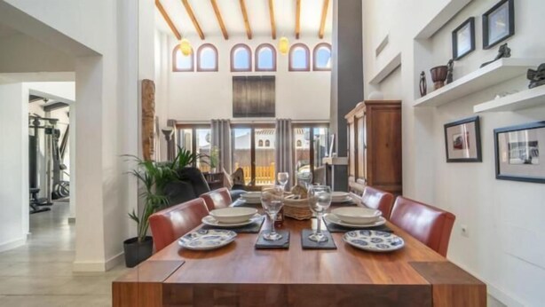Un espace repas avec une longue table en bois, dressée pour six personnes, entourée de chaises en cuir.