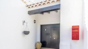 Une terrasse carrelée avec une porte, une boîte aux lettres et un petit vase décoratif.