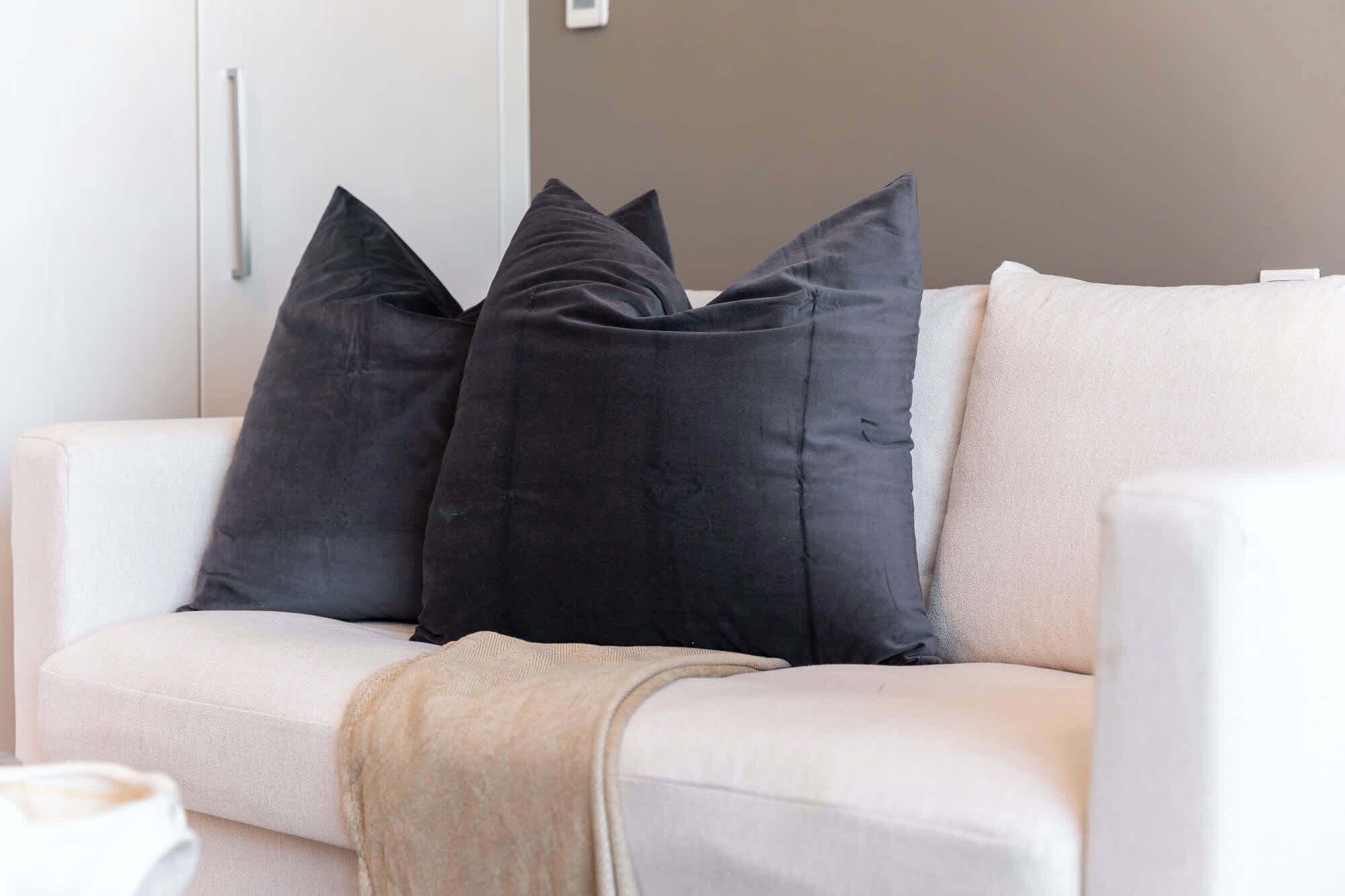 A white sofa with three black pillows and a beige throw blanket.