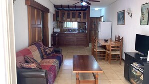Ein Wohnzimmer mit einer Couch, einem Holztisch, einer TV-Konsole und einem Essbereich mit Tisch und Stühlen.