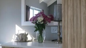 Une cuisine moderne avec un plan de travail blanc, un évier encastré et un grand miroir au-dessus de l’évier. Un vase rempli de fleurs est posé sur le plan de travail.