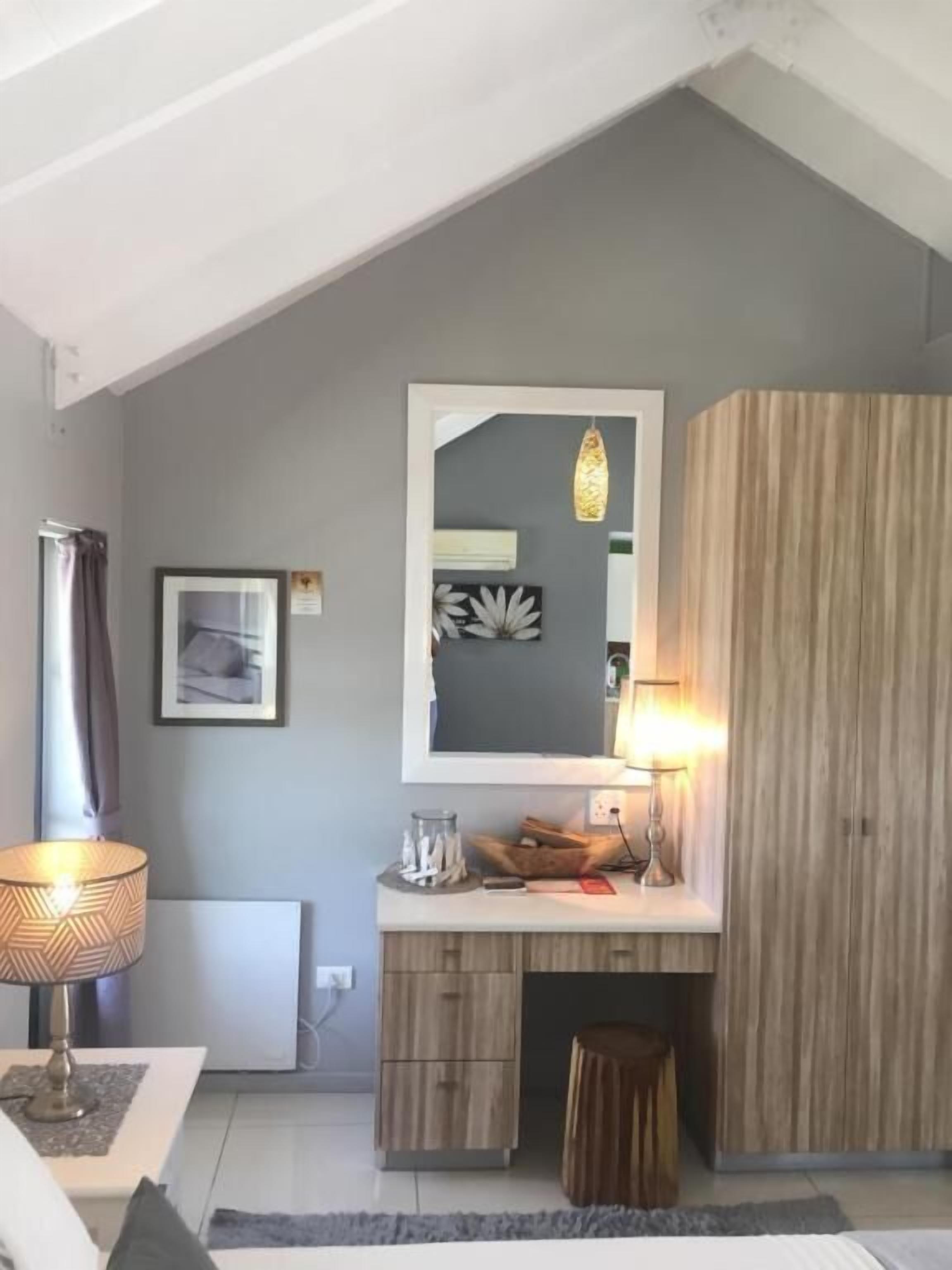 Ein modernes Schlafzimmer mit schrägen Wänden, einem großen Spiegel, einer Nachttischlampe, einem Holzschrank und einem kleinen Hocker.