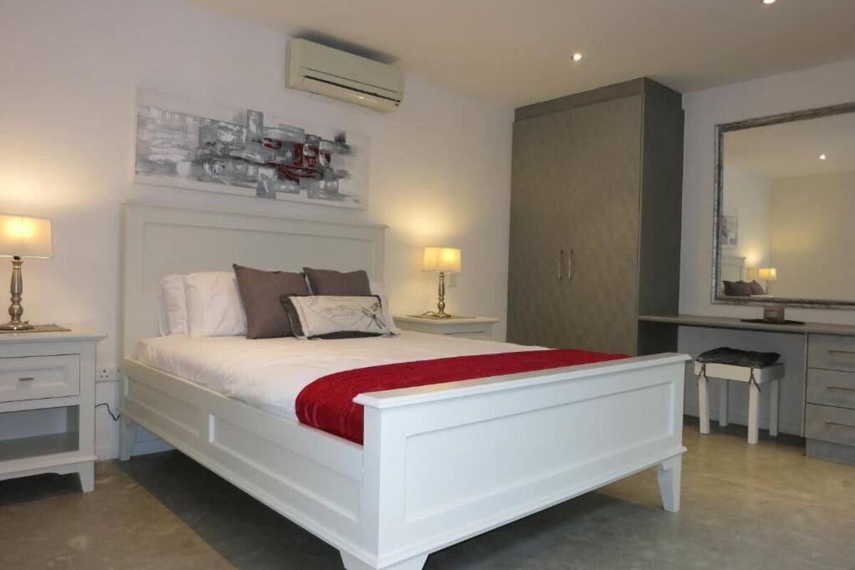 Quarto com cama branca, duas mesas de cabeceira com luminárias, um guarda-roupa grande e um espelho.