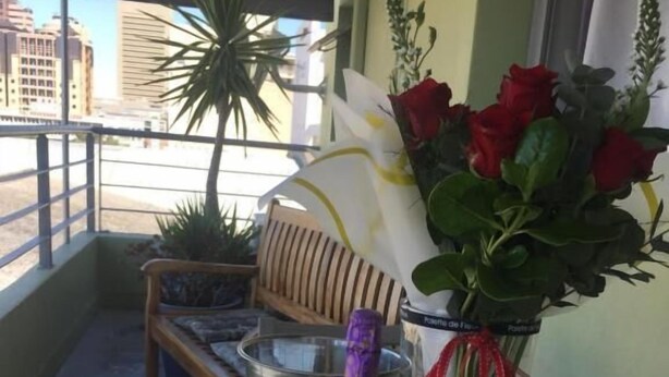 A balcony with a table set for two, featuring two wine glasses, a bottle of champagne, and a bouquet of red roses. - Man And Tree House  (Cape Town)
