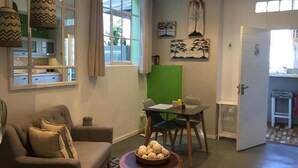 A living room with a sofa, a dining table with chairs, a coffee table with decorative items, and a green partition wall. - Man And Tree House  (Cape Town)