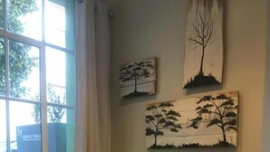 A room with a table, two chairs, a window with a view of trees, and wall art depicting trees. - Man And Tree House  (Cape Town)