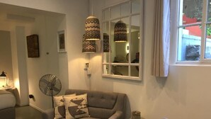 Un salon chaleureux avec un canapé gris, une table à manger ornée d’une bougie jaune et une fenêtre donnant sur un immeuble rouge.