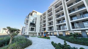 A multi-story residential building with balconies, a playground, and landscaped areas. - Modern 1-Bedroom Apartment With Padel Court Access (Arjan)