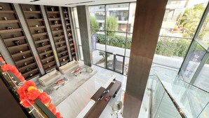 A modern reception area with a marble reception desk, two sofas, and a large glass window offering a view of the outdoor area. - Modern 1-Bedroom Apartment With Padel Court Access (Arjan)