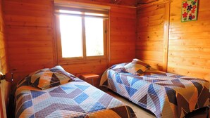Une cabane avec deux lits, des murs en bois, une fenêtre et un élément décoratif mural.
