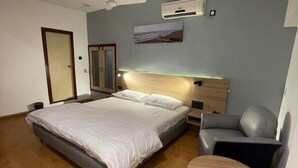 A bedroom with a bed, a chair, a small table, and a ceiling fan. - Hotel Bengal International (Siliguri)