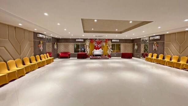 A spacious hall with rows of yellow chairs, a central stage with red curtains, and decorative floral arrangements. - Hotel Bengal International (Siliguri)