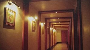 A long, narrow hallway with framed artwork on the walls and a polished floor. - Hotel Bengal International (Siliguri)