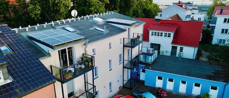 A multi-story residential building with balconies, solar panels, and a parking area with cars.