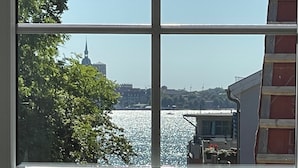 A view through a window with a clear sky, a body of water, and a distant building with a spire. - Living with a harbor view—200 meters from the South Beach on the island of Rügen (Altefähr)