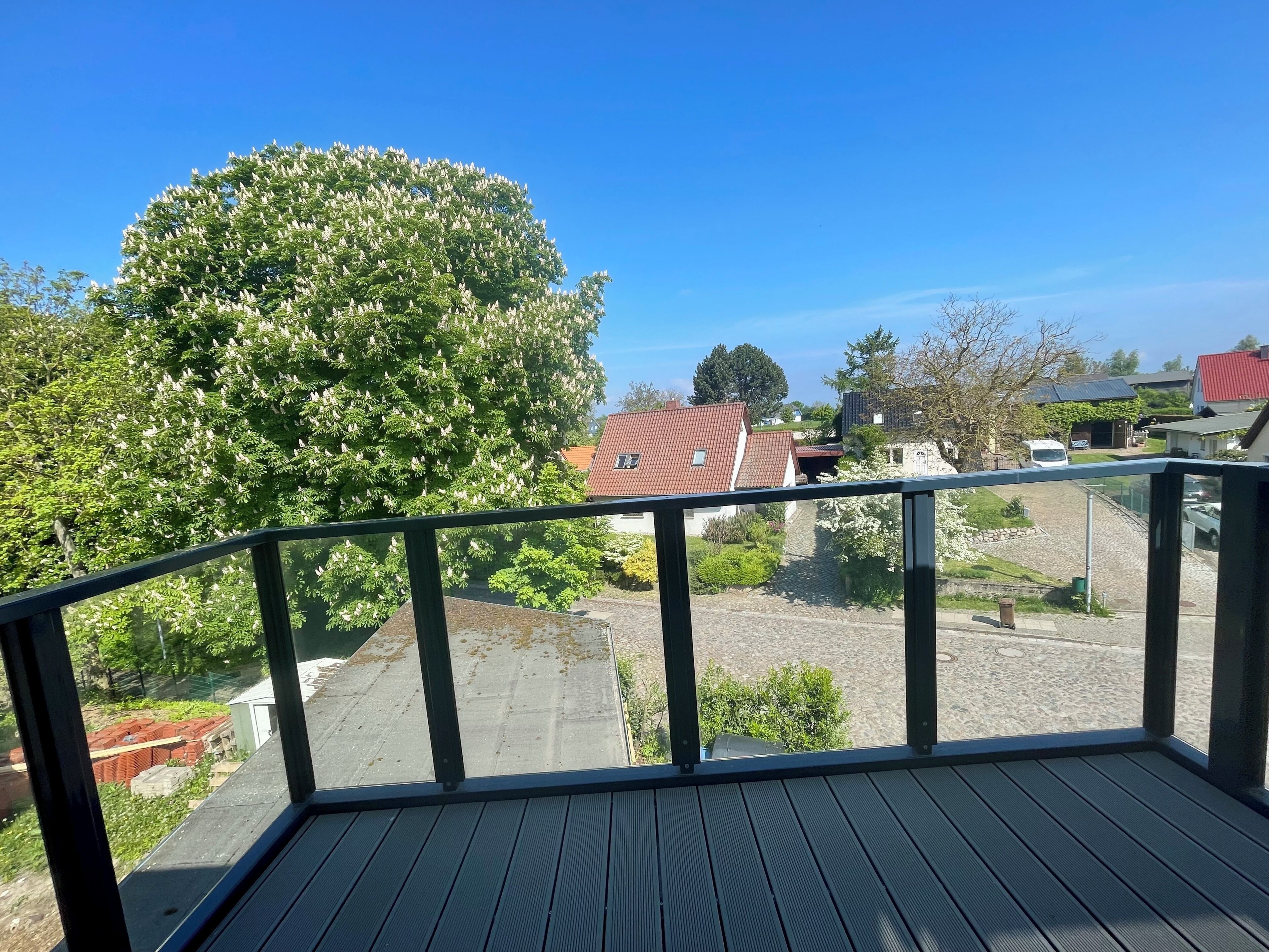 Een balkon met uitzicht op een woonwijk, met huizen en een grote boom.