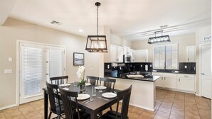 A modern kitchen with white cabinets, a black countertop, and a dining area with a dark table and chairs. - 4-bedroom, 3 Bath Home in Gilbert—Pets Welcome  (Gilbert)