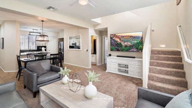 A modern living room with a grey sofa, a coffee table with decorative vases, a flat-screen TV mounted on the wall, and a staircase leading to another level. - 4-bedroom, 3 Bath Home in Gilbert—Pets Welcome  (Gilbert)