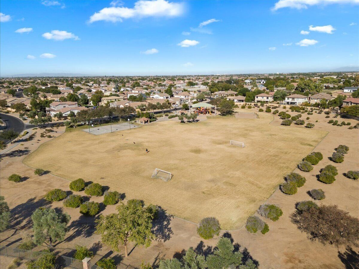 Vista aérea de una zona residencial con casas, un campo abierto grande con un arco de fútbol y árboles dispersos.