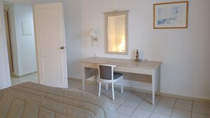 A hotel room with a bed, a desk, a chair, a mirror, and a picture on the wall.