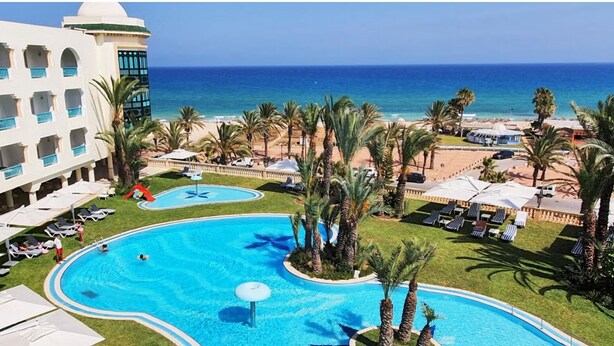 A resort with a large pool, palm trees, and a view of the ocean.