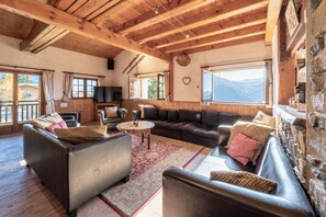 A cozy living room with wooden beams, leather sofas, a TV, and a view of mountains. - Authentic CHALET 15 people "LA BERGERIE" - La Rosière 1850 (Montvalezan)