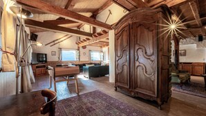 A spacious living room with wooden beams, a large wooden cabinet, a pool table, and a cozy seating area.