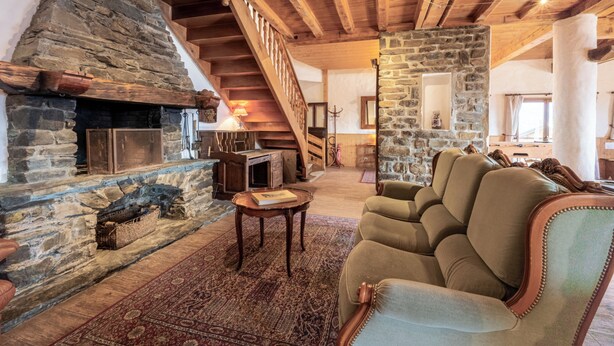 A cozy living room with a stone fireplace, wooden beams, a staircase, and a comfortable sofa.