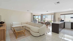 A modern living room with a sectional sofa, a glass-top coffee table, and a dining area with chairs. - 15 Offshore Dr Middleton - Wi-Fi and Linen Included (Middleton)