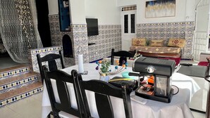 Un comedor con una mesa lista para cuatro personas, una cafetera y una planta decorativa.