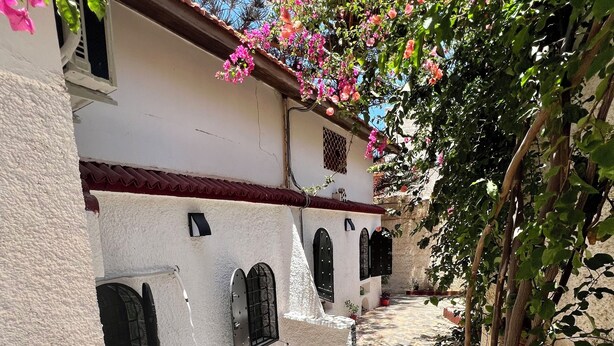 Un patio estrecho con un edificio blanco que presenta puertas arqueadas y suelo de baldosas.