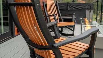 Una mecedora de madera y una mesa en una terraza con cerramiento de vidrio, con vistas a un paisaje natural.