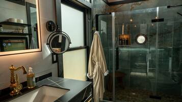 Een moderne badkamer met een douchecabine van glas, een wastafel met een gouden kraan en een handdoek aan de muur.