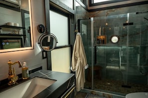 A modern bathroom with a glass-enclosed shower, a vanity with a gold faucet, and a towel hanging on the wall.
