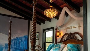 Une chambre à coucher avec un lit à baldaquin, un lustre, une grande fenêtre et une fresque représentant un navire sur le mur.