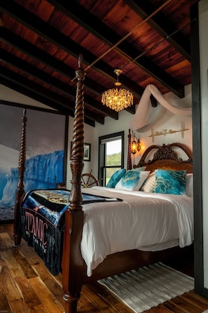 A bedroom with a four-poster bed, a chandelier, a large window, and a mural of a ship on the wall.
