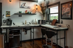 A kitchen with a Galanz refrigerator, a microwave, and a sink. There are two black chairs and a window with a view.