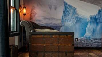Un dormitorio con un amplio mural de hielo, un cofre de madera, un sillón de cuero y una lámpara de pared.