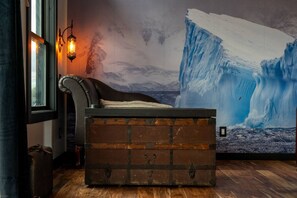 A bedroom with a large ice wall mural, a wooden chest, a leather chair, and a wall-mounted lamp. - Jack & Rose Treehouse Titanic Hot tub Riverfront. (Sevierville)