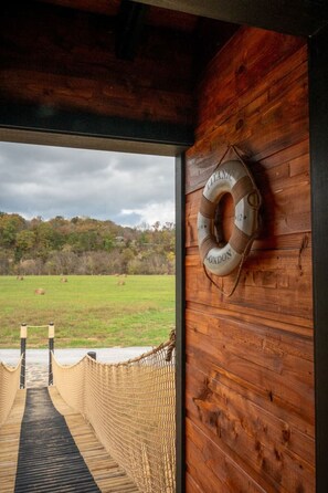 A wooden interior with a lifebuoy on the wall and a view of a grassy field through a wooden door.