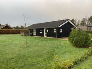 Un bâtiment noir avec un toit en pente, une petite pelouse et une haie.